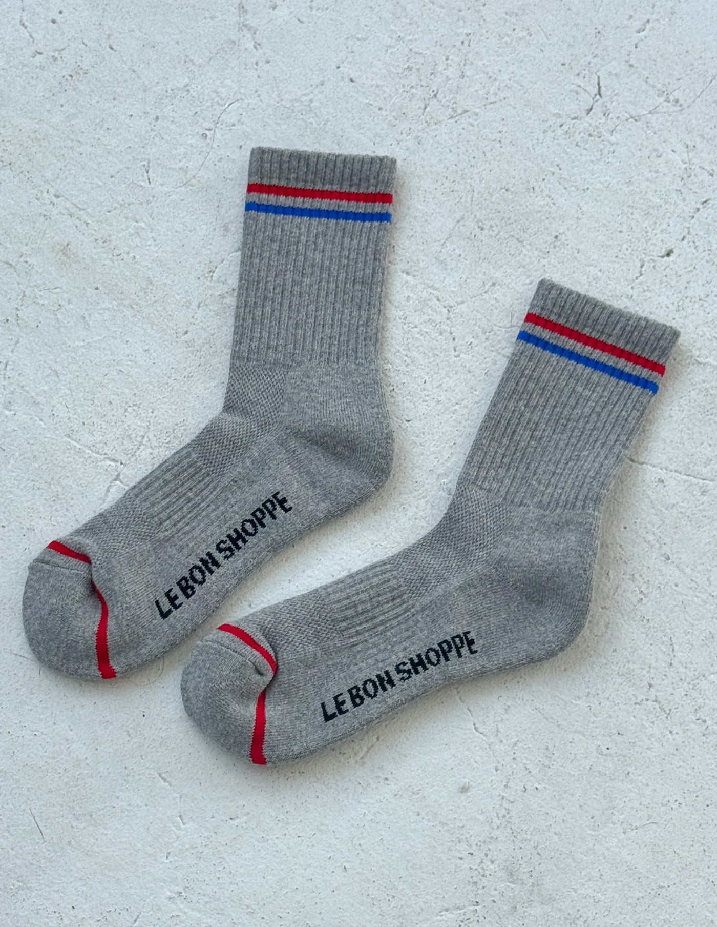 Gray socks with red and blue stripes and 'Le Bon Shoppe' branding on a light gray background