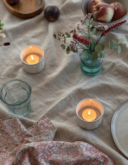 Candlelit table setting with flowers, glasses, and a floral cloth on a textured surface.