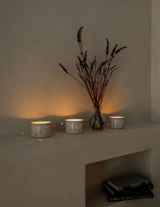 Three lit candles on a shelf with a vase of dried lavender against a neutral wall.