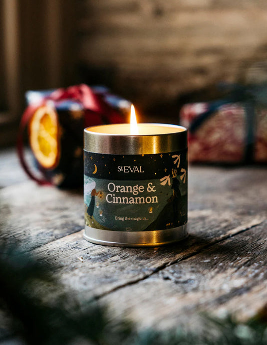 Candle labeled 'Orange & Cinnamon' by SVEVAL on a wooden surface with decorative items in the background.
