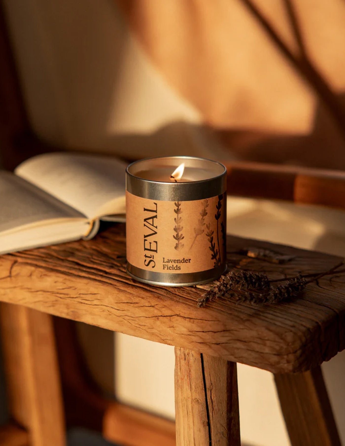 St. Eval Lavender Fields candle on a wooden surface with an open book and dried lavender.