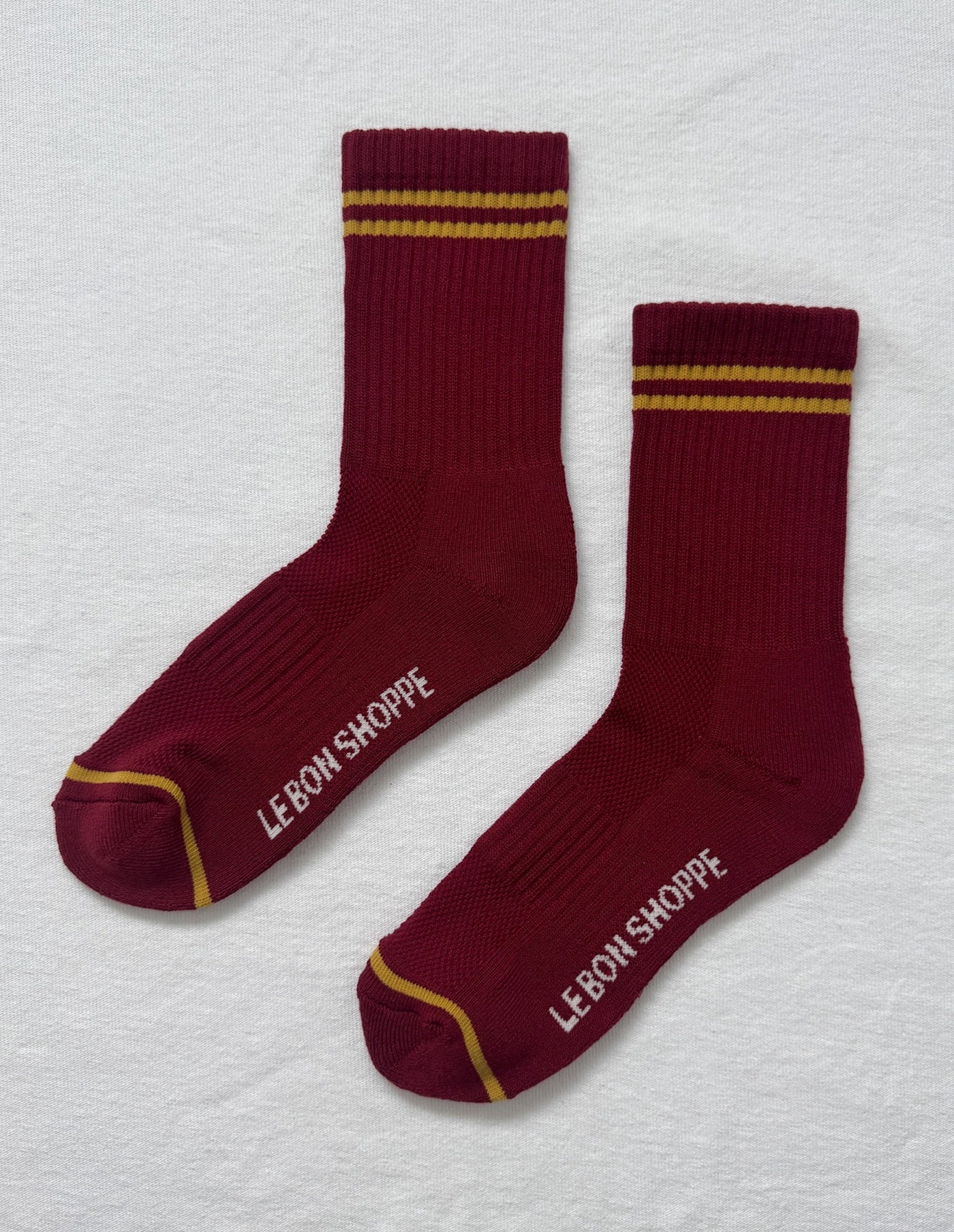 Maroon socks with gold stripes and 'Lebon Shoppe' branding on a light gray background