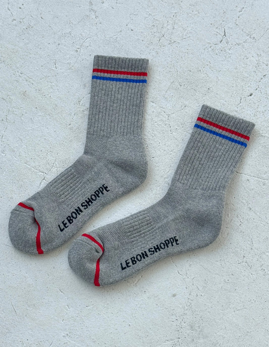 Gray socks with red and blue stripes and 'Le Bon Shoppe' branding on a light gray background