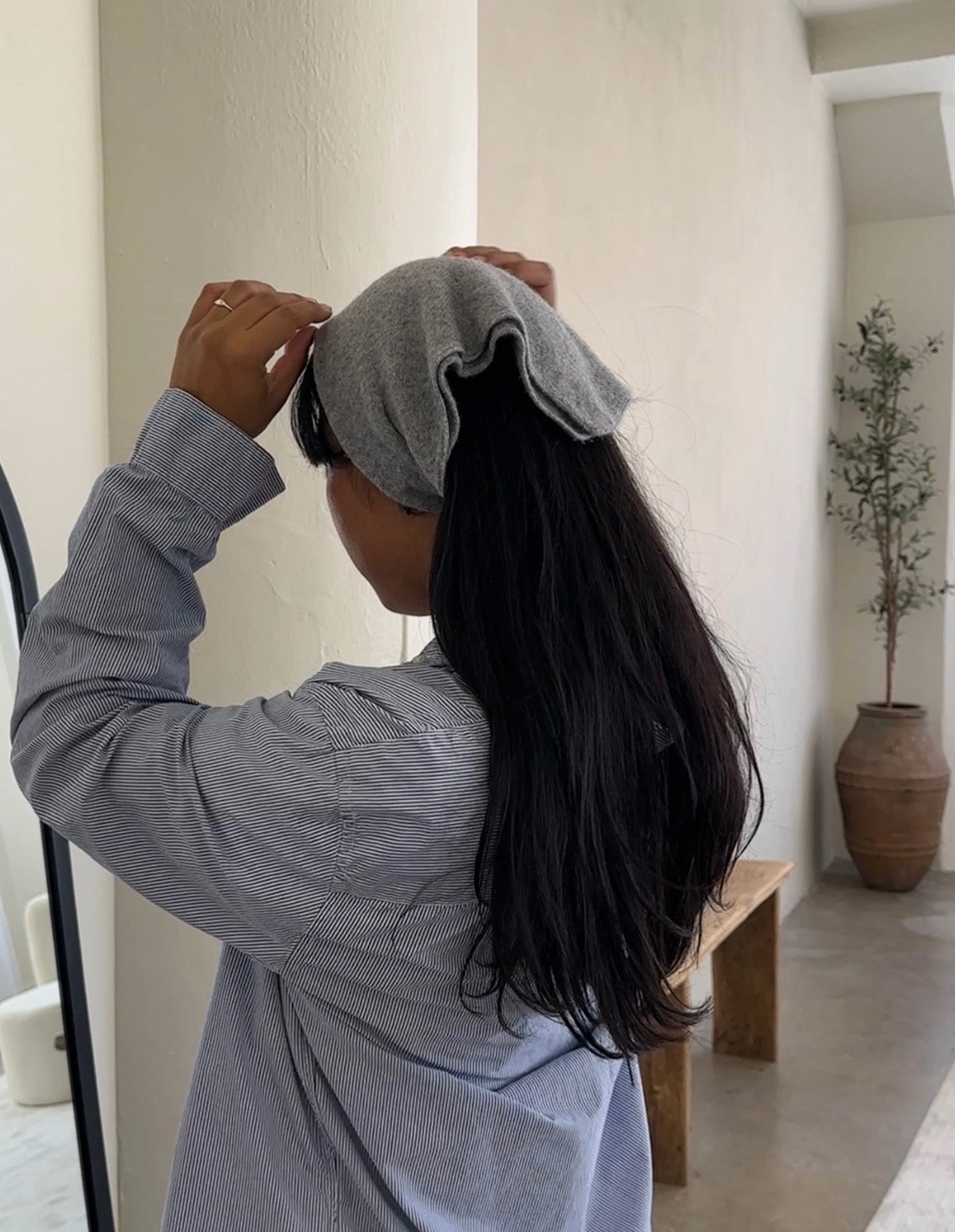 Person wearing a gray hair towel in a room with a plant and bench.