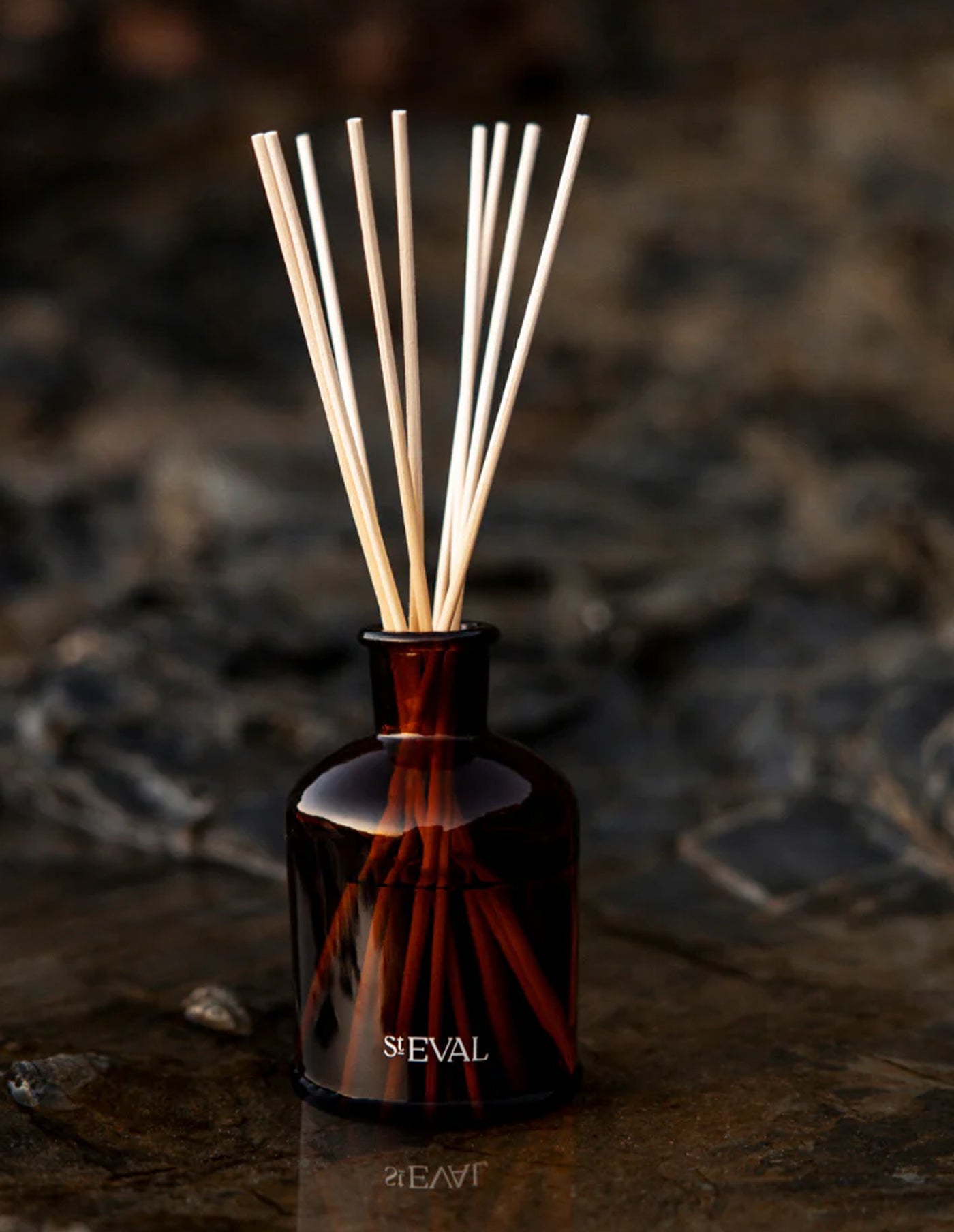 Brown glass diffuser bottle with wooden sticks on a textured surface