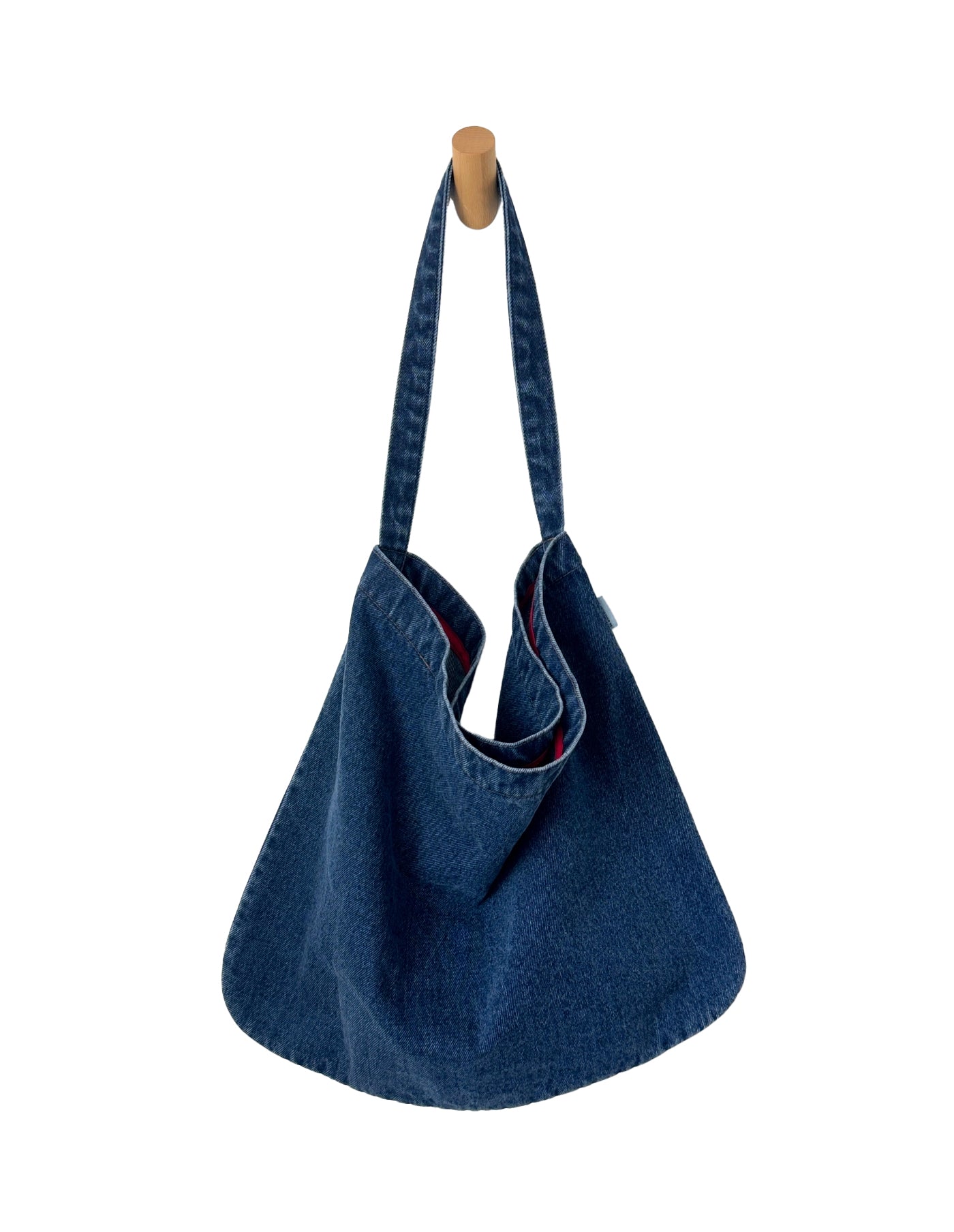 Blue denim handbag hanging on a wooden hook against a white background