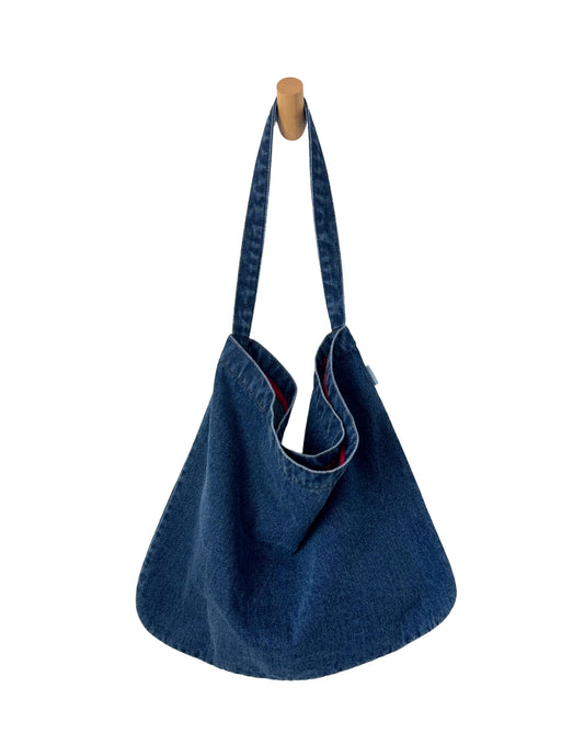 Blue denim handbag hanging on a wooden hook against a white background