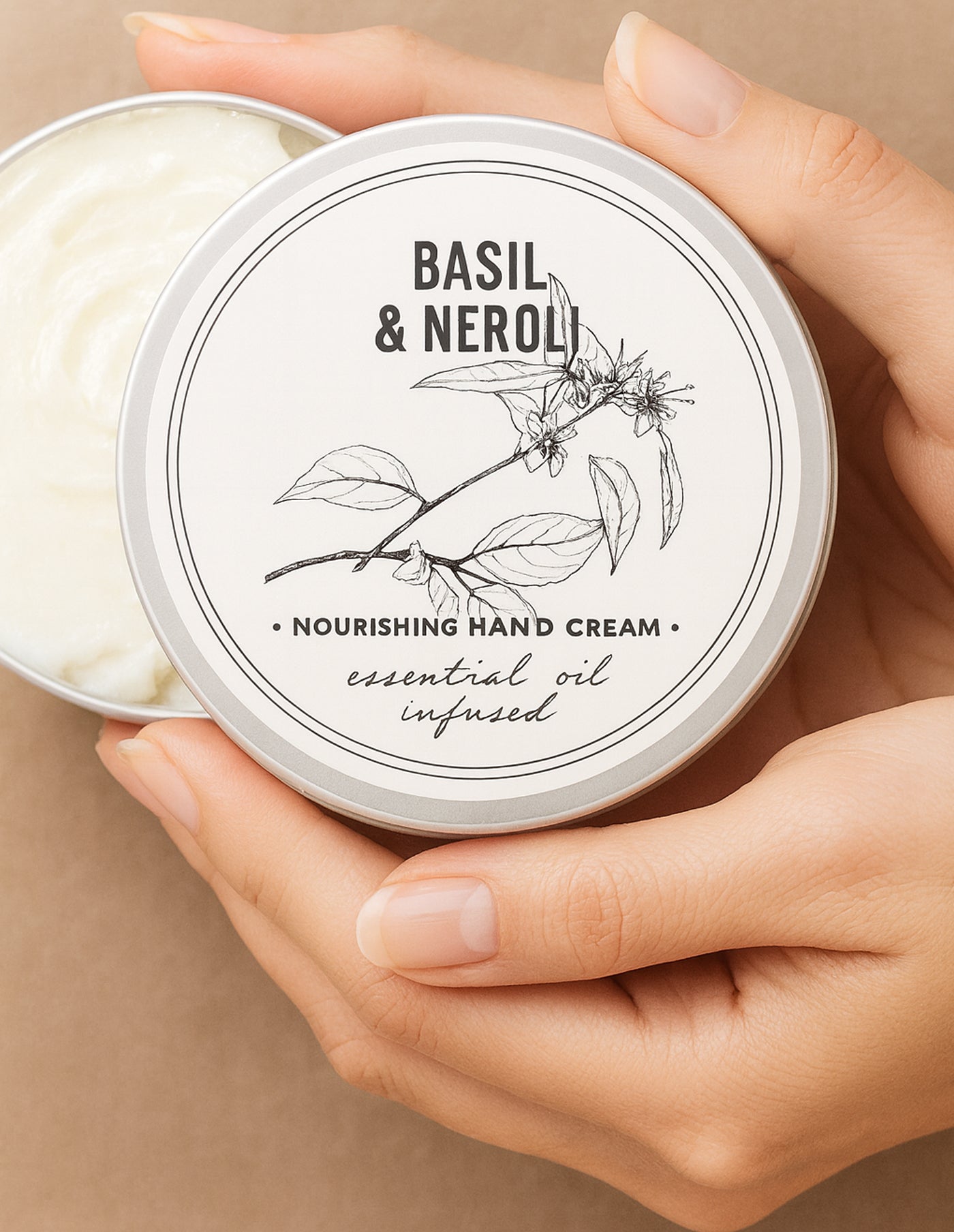 Basil & Neroli hand cream in a tin held by hands against a beige background