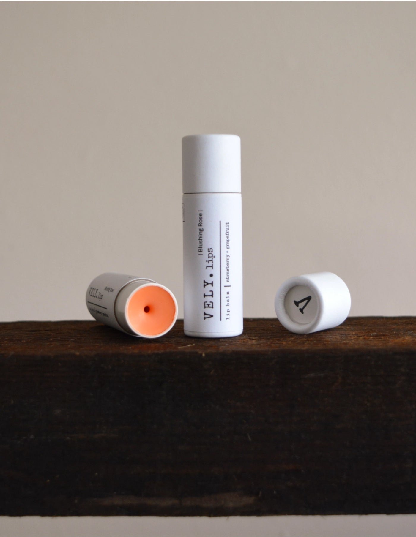 Three lip balm tubes with visible brand 'VELV' on a wooden surface.