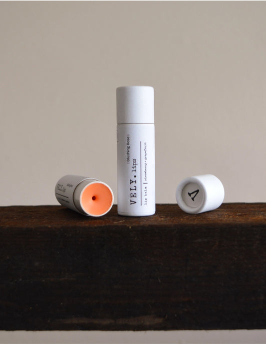 Three lip balm tubes with visible brand 'VELV' on a wooden surface.