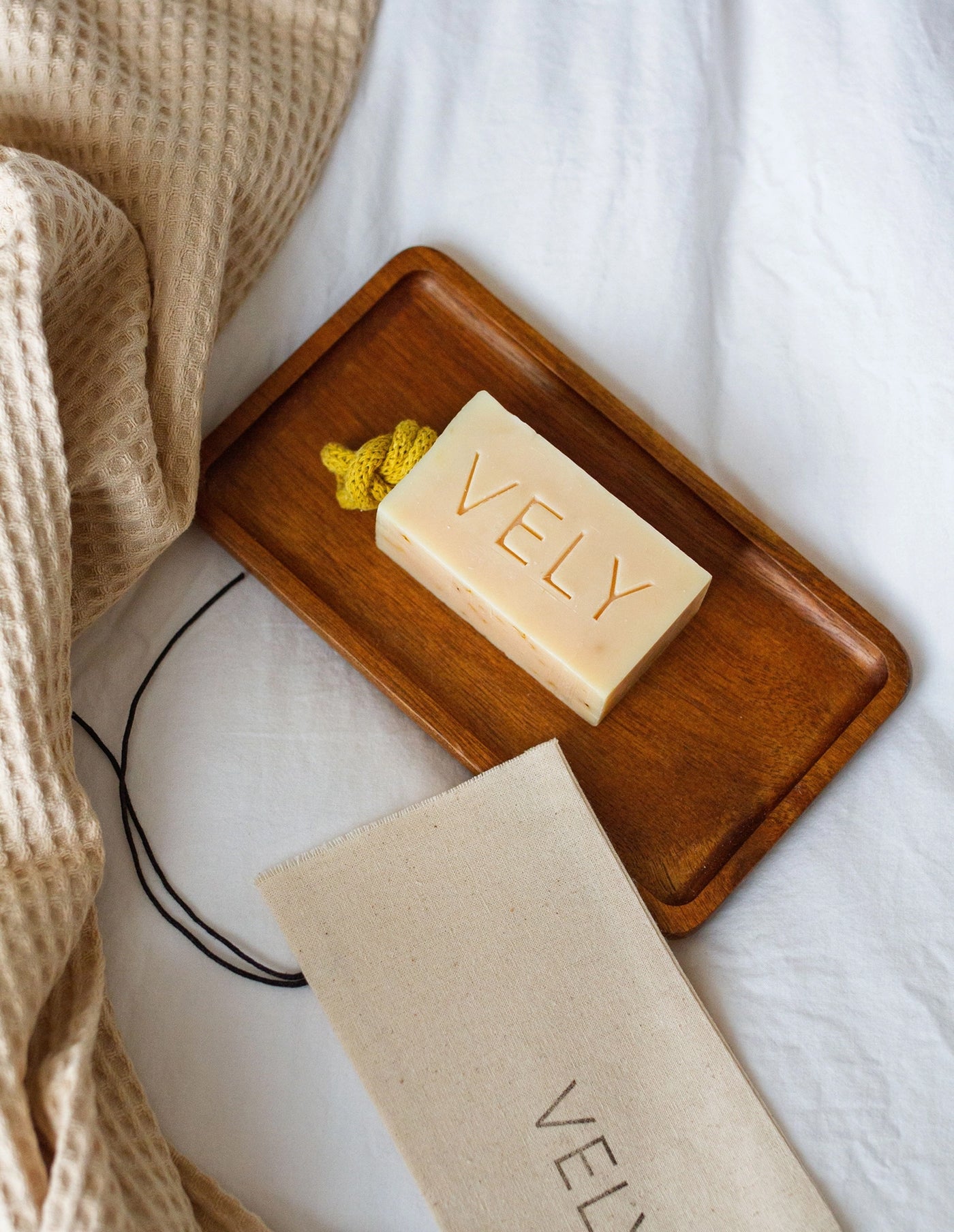Bar of soap with 'VELY' branding on a wooden tray on a white surface.