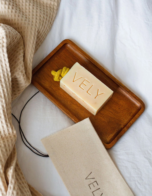 Bar of soap with 'VELY' branding on a wooden tray on a white surface.