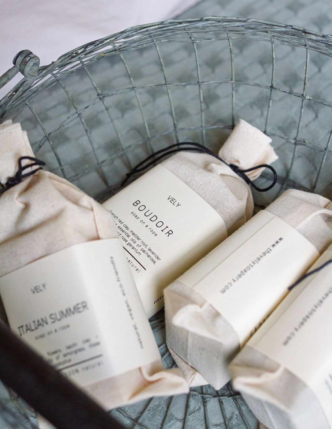 Bars of soap in decorative paper packaging with visible branding on a wire basket.